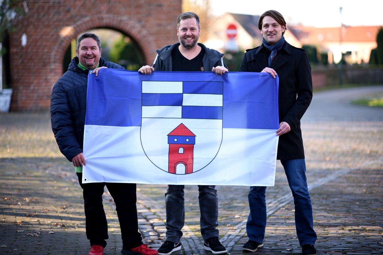 750 Jahre Wardenburg - das OrgaTeam Marktplatz Oliver Bremer und Jan Meiners mit Kulturbeauftragtem Hendrik Müller und der Wardenburgflagge. Foto: Wolfgang Hitschler 750 Jahre Wardenburg - das OrgaTeam Marktplatz Oliver Bremer und Jan Meiners mit Kulturbeauftragtem Hendrik Müller und der Wardenburgflagge. Foto: Wolfgang Hitschler