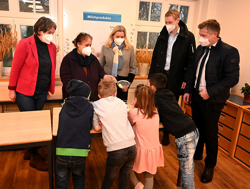 Hauswirtschafterin Seher Hamdan (2.v.l.) bringt Kindern der Grundschule Deichhorst sowie (v.r.) Landrat Dr. Christian Pundt, Bürgermeister Ralf Wessel, Oberbürgermeisterin Petra Gerlach und Marina Becker Kückens (l.) die Herstellung von Butter näher. Foto: Gemeinde Ganderkesee | Hauke Gruhn